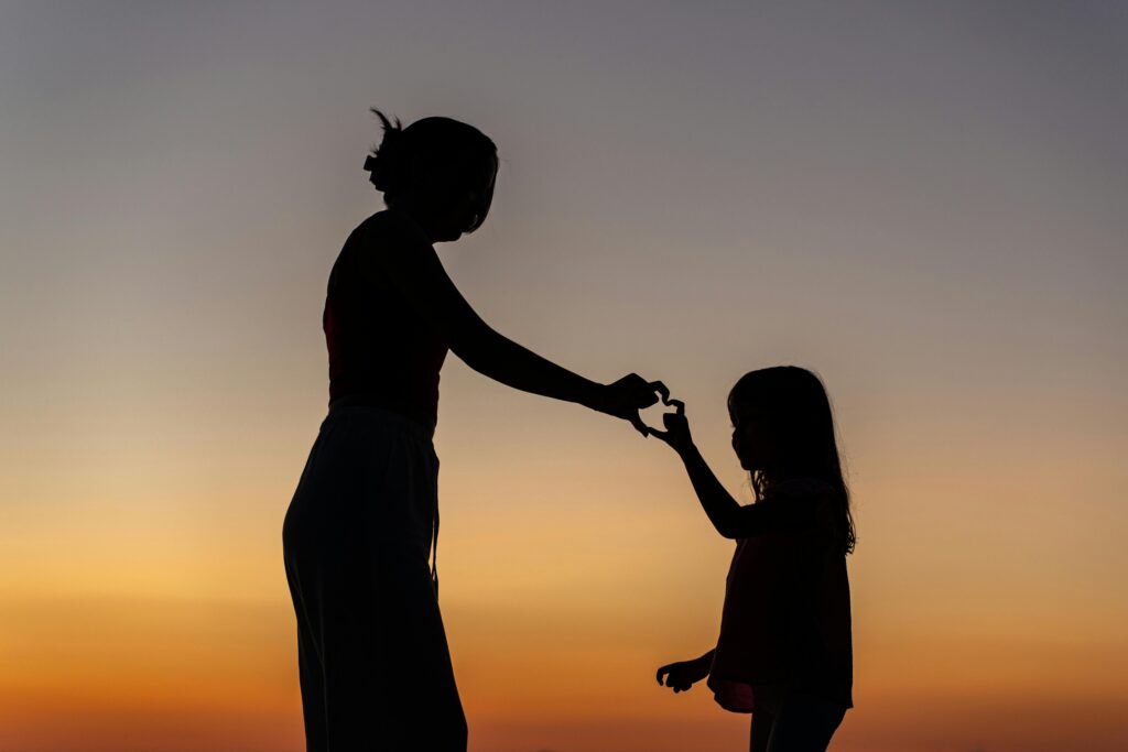 Silhouette of a woman and child holding hands at sunset