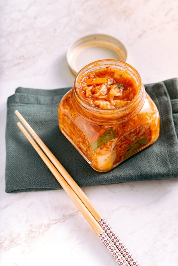 pexels-photo-6823261-6823261 A jar of traditional homemade kimchi on a marble surface with wooden chopsticks beside it.
