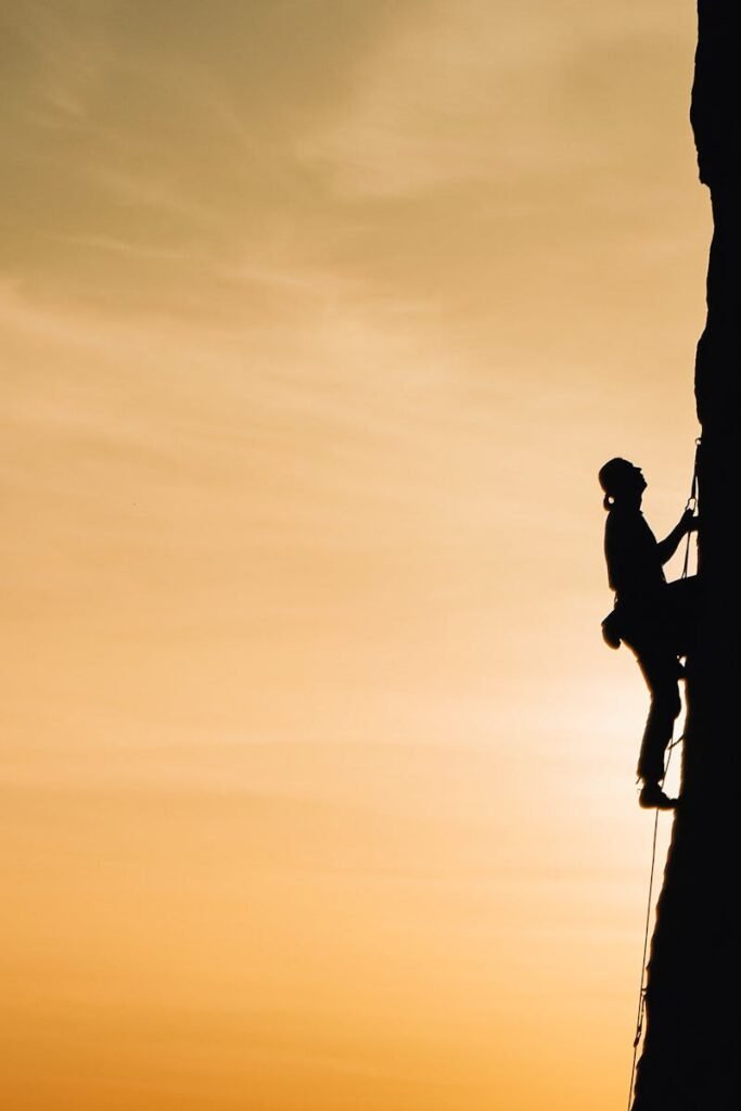 A silhouette of a rock climber scaling a steep cliff during sunset in Russia, showcasing determination and adventure.