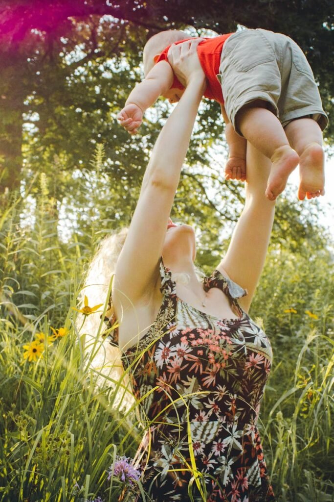 A joyful mother lifts her baby in a sunny summer meadow, capturing a moment of love and happiness.