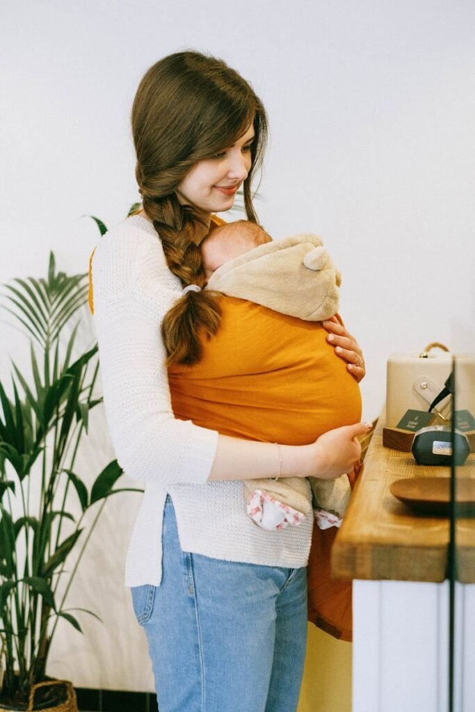 A warm moment of a mother holding her baby in a sling inside a cozy cafe.