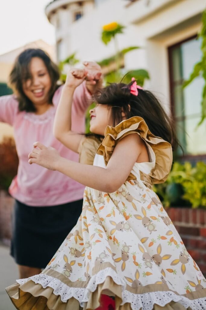 pexels-photo-5637809-5637809 A mother dances with her twin daughters in a lively outdoor setting, enjoying a sunny day.