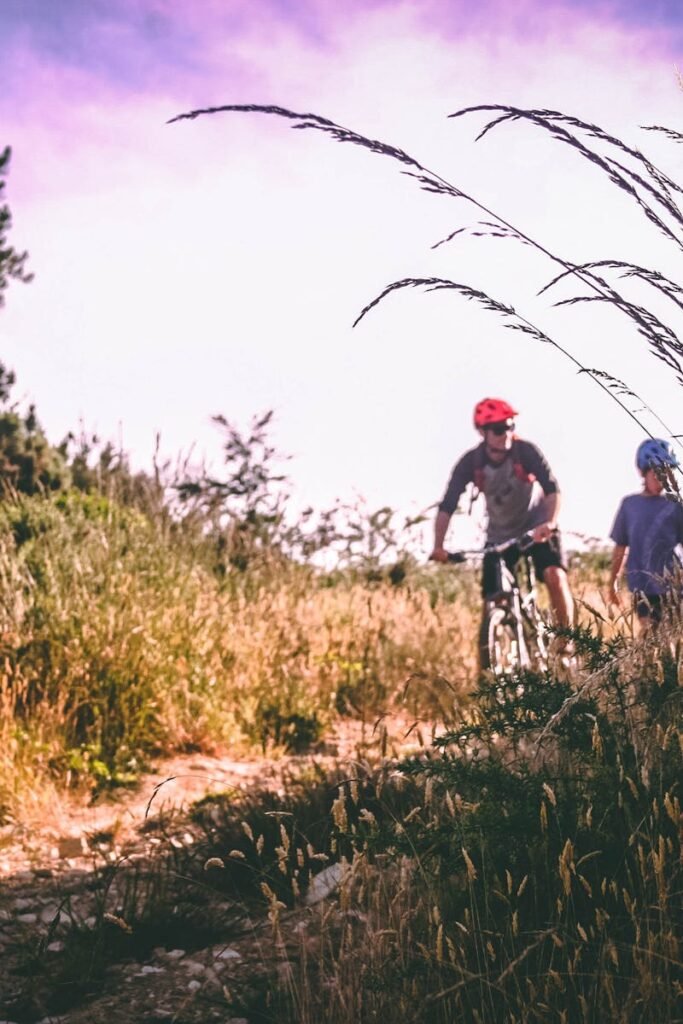 pexels-photo-733739-733739 A father and child enjoy mountain biking on an unpaved path surrounded by tall grass and trees.